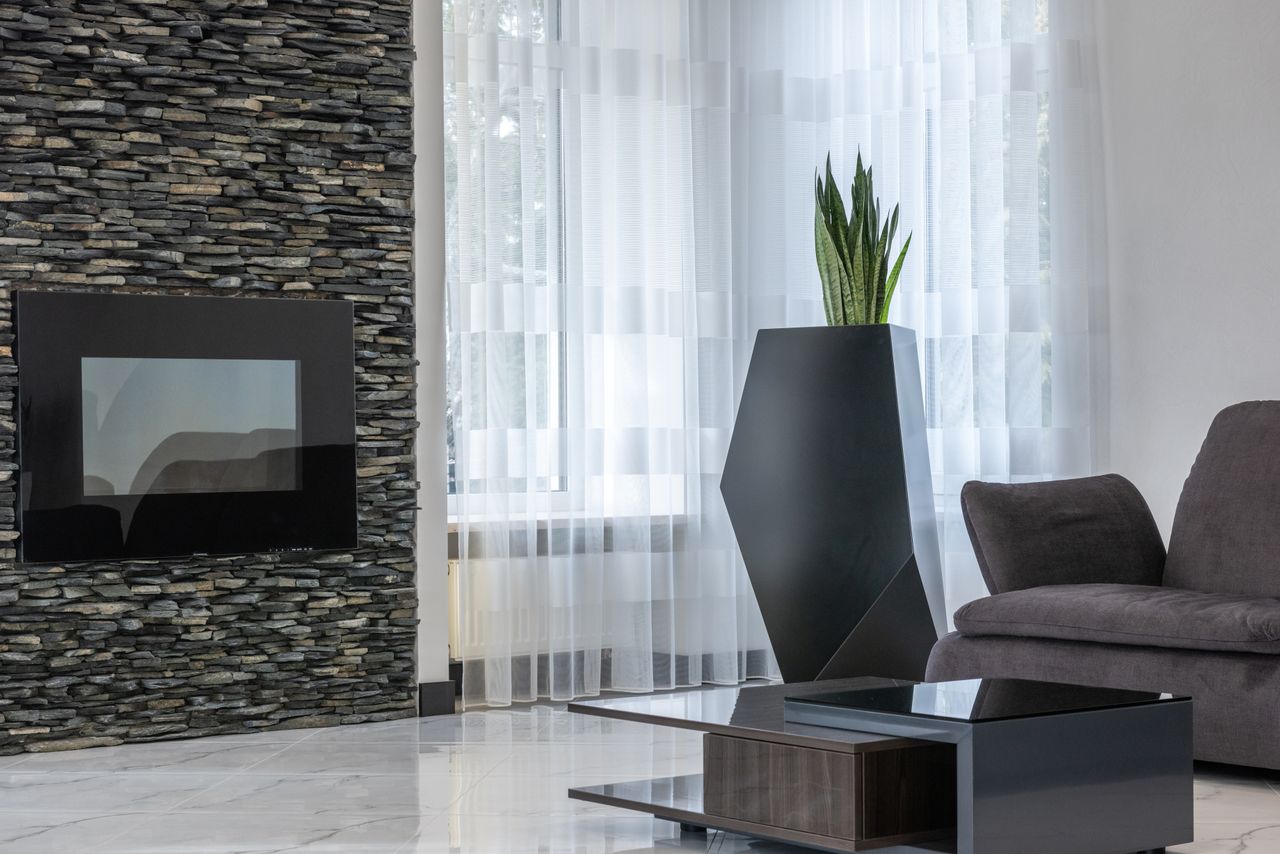 About Electric fireplace on creative stone wall in spacious modern living room with cozy sofa and exotic potted plant