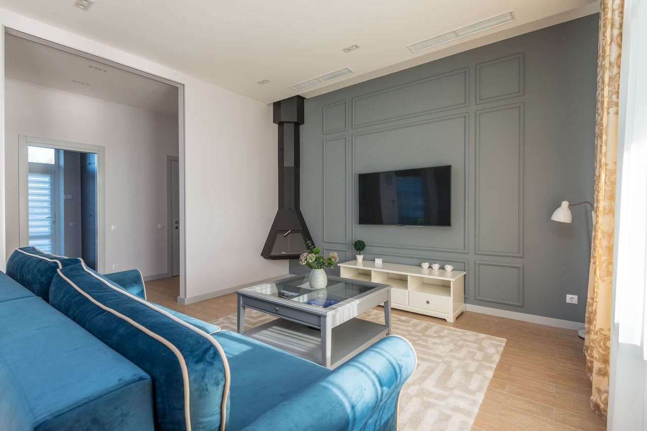 Services A stylish living room featuring a blue couch, wall-mounted TV, and elegant decor.