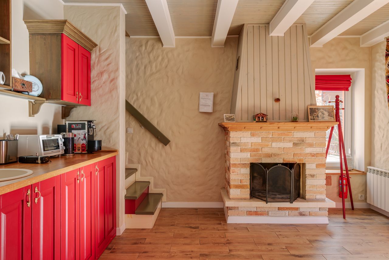 Mastering the First Impression: Your intriguing post title goes here Warm rustic kitchen interior with vibrant red cabinets and a charming brick fireplace for a cozy home feel.